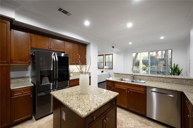 kitchen with light stone counters, visible vents, a sink, a kitchen island, and stainless steel appliances
