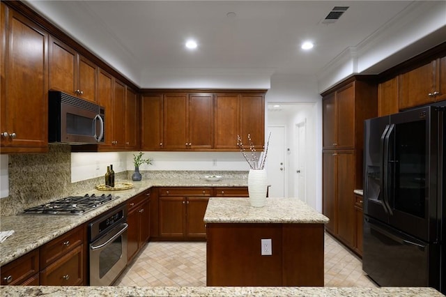 kitchen with appliances with stainless steel finishes, a kitchen island, light stone countertops, and visible vents