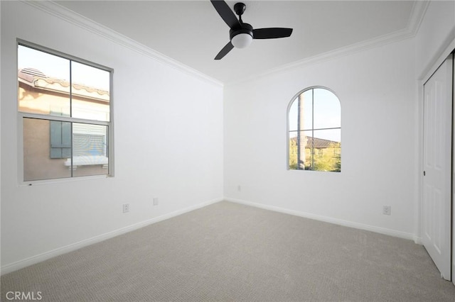 carpeted spare room with a ceiling fan, baseboards, and crown molding
