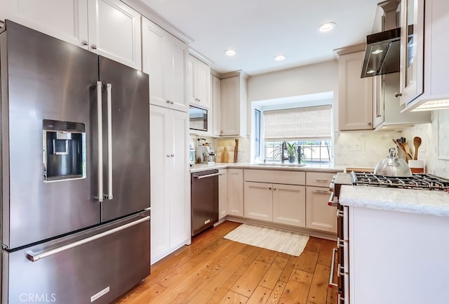 kitchen with high end appliances, light wood-type flooring, decorative backsplash, and a sink
