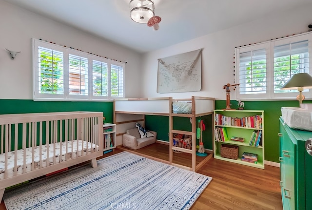 bedroom featuring baseboards, a nursery area, and wood finished floors