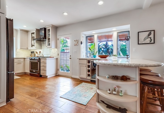 kitchen with wine cooler, open shelves, wall chimney exhaust hood, light wood-style flooring, and stainless steel range