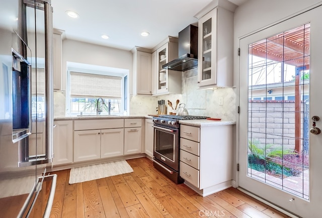 kitchen with high end stove, wall chimney exhaust hood, light wood-style floors, and a sink
