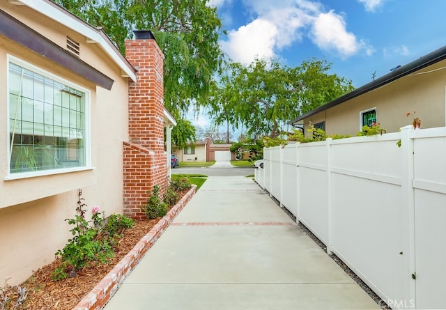 view of side of property featuring stucco siding, a chimney, and fence