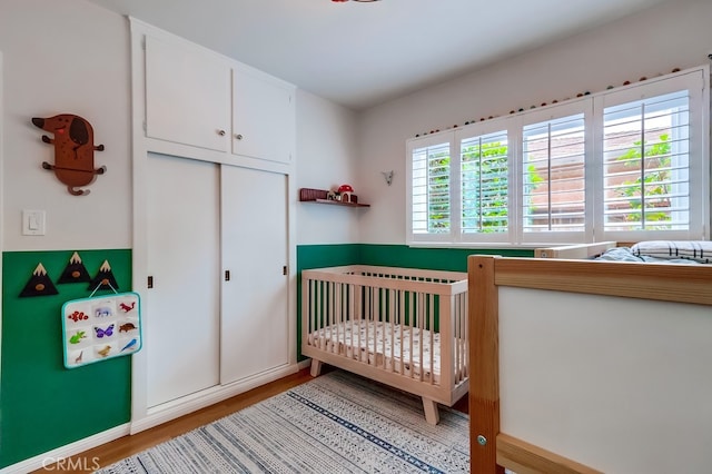 bedroom featuring baseboards, a nursery area, a closet, and wood finished floors