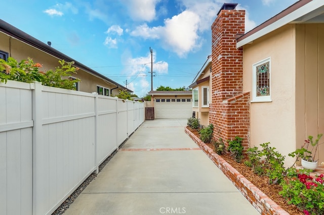 view of side of home with a chimney, an outbuilding, fence, a garage, and stucco siding