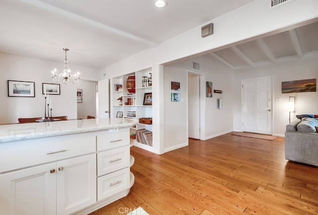 kitchen with light wood-style flooring, white cabinetry, a notable chandelier, and light stone counters