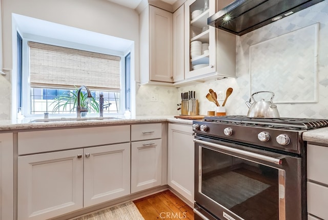 kitchen featuring a sink, extractor fan, white cabinets, stainless steel range with gas cooktop, and decorative backsplash