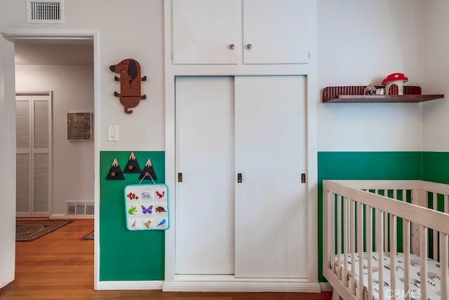 unfurnished bedroom with a nursery area, a closet, visible vents, and wood finished floors