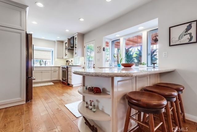 kitchen featuring light wood finished floors, wall chimney exhaust hood, open shelves, and appliances with stainless steel finishes
