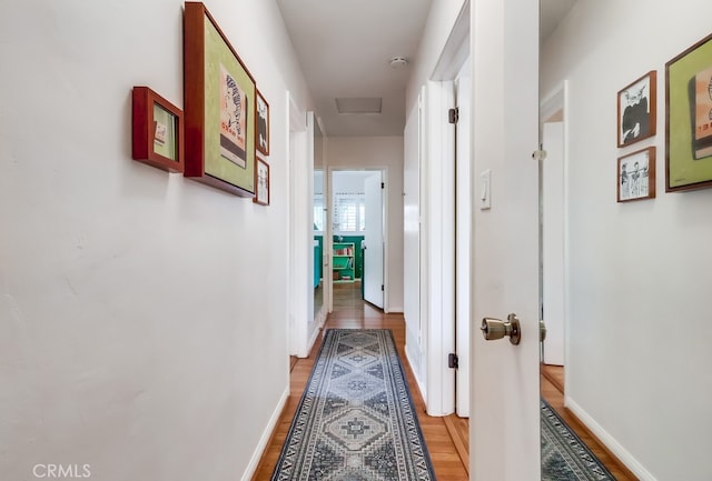 hallway with baseboards, attic access, and wood finished floors
