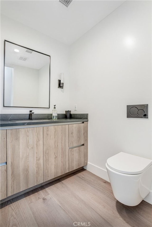 bathroom with toilet, baseboards, double vanity, and wood finished floors
