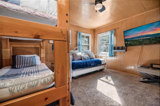 bedroom with ceiling fan, wooden walls, and carpet flooring