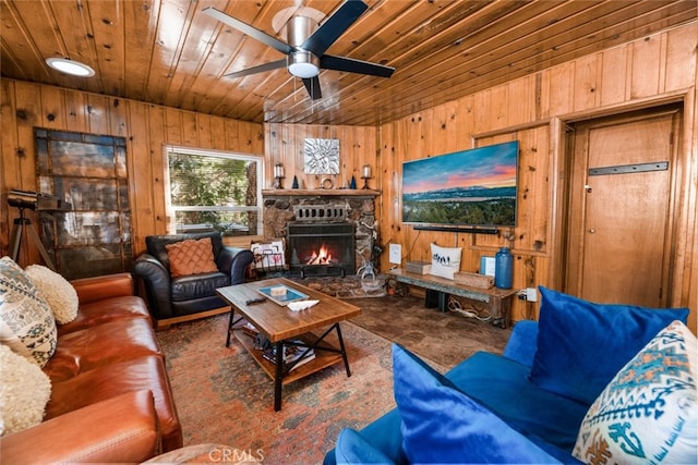 living room featuring a ceiling fan, a stone fireplace, wooden walls, and wood ceiling