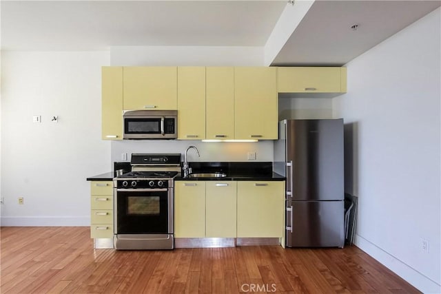 kitchen featuring cream cabinets, a sink, dark countertops, stainless steel appliances, and light wood-type flooring