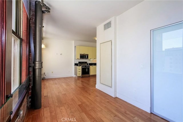 hall with light wood-style flooring, baseboards, and visible vents