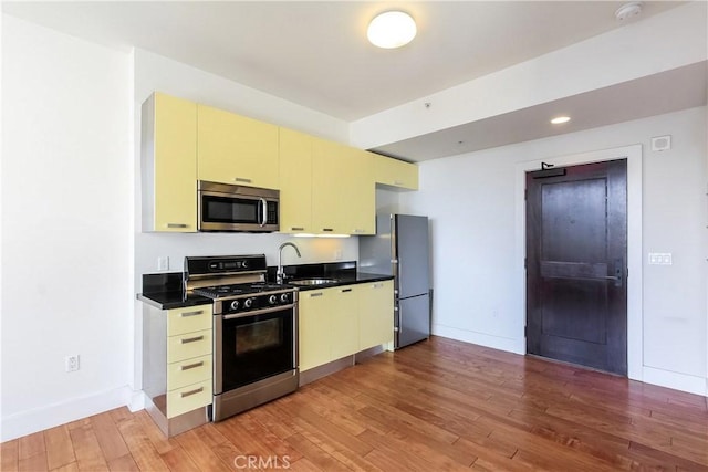 kitchen with a sink, freestanding refrigerator, cream cabinetry, gas range, and stainless steel microwave