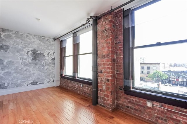 spare room featuring baseboards, brick wall, and wood finished floors