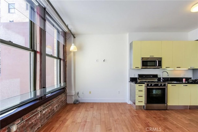 kitchen with dark countertops, appliances with stainless steel finishes, cream cabinets, and light wood-style flooring