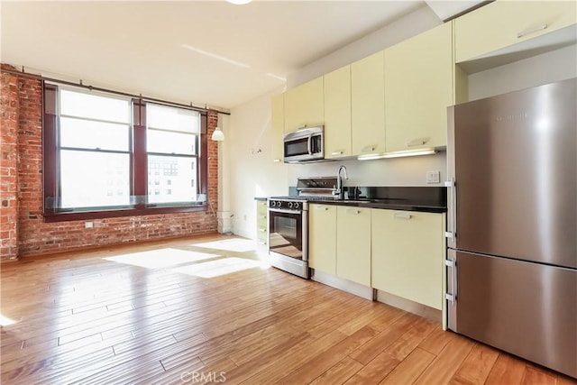 kitchen featuring light wood finished floors, stainless steel appliances, cream cabinetry, and dark countertops