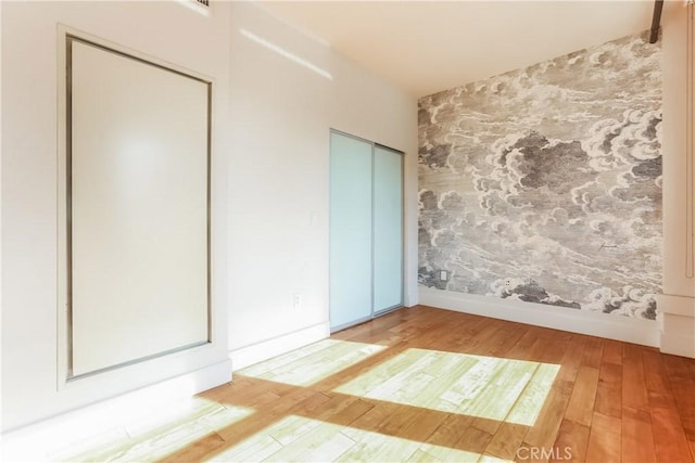 unfurnished bedroom featuring wallpapered walls, wood finished floors, baseboards, and multiple closets