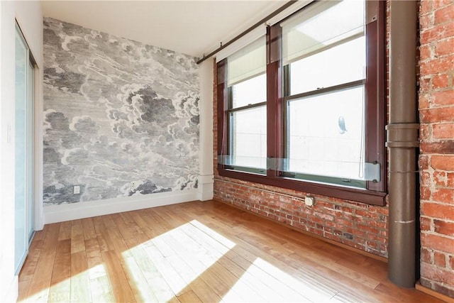 spare room with brick wall, wood-type flooring, and baseboards