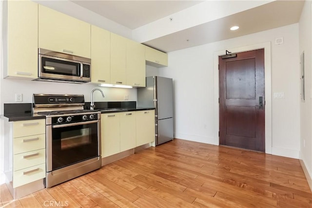 kitchen with freestanding refrigerator, a sink, stainless steel microwave, gas range, and cream cabinets