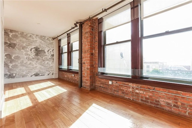 empty room featuring a wealth of natural light, baseboards, wallpapered walls, and wood finished floors