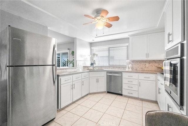 kitchen featuring a ceiling fan, a sink, stainless steel appliances, white cabinets, and tasteful backsplash