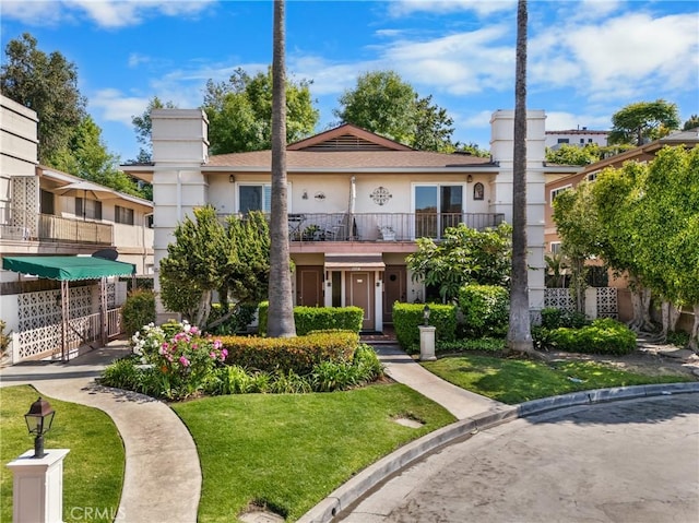 view of front of property featuring a balcony, stucco siding, and a front lawn