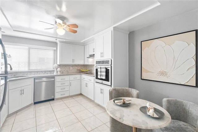 kitchen featuring a ceiling fan, a sink, stainless steel appliances, white cabinetry, and backsplash