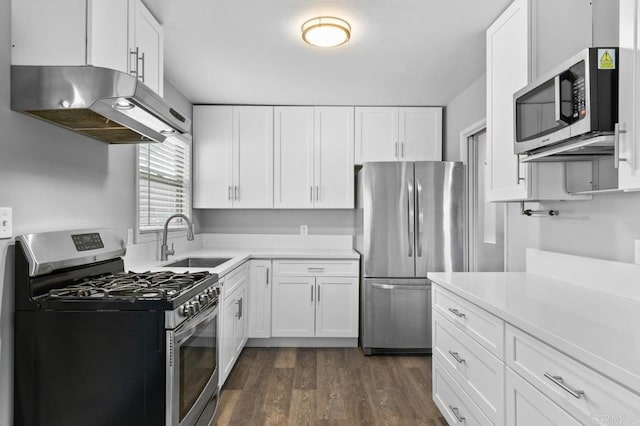 kitchen with a sink, white cabinets, under cabinet range hood, appliances with stainless steel finishes, and dark wood-style floors