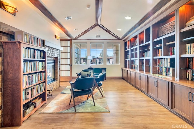 sitting room with baseboards, a stone fireplace, light wood finished floors, visible vents, and lofted ceiling with beams