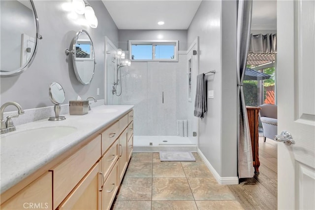full bathroom featuring a stall shower, baseboards, double vanity, and a sink