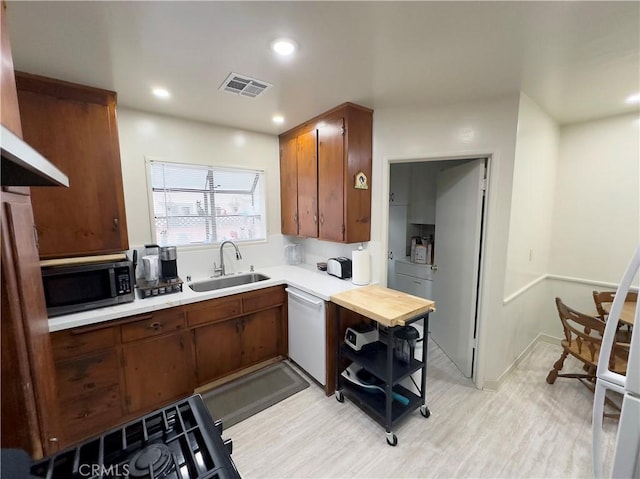 kitchen with a sink, stainless steel microwave, visible vents, light countertops, and white dishwasher