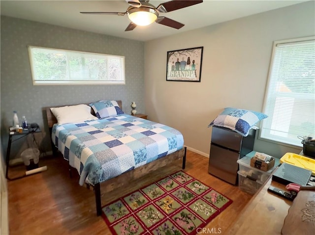bedroom with wallpapered walls, baseboards, wood finished floors, and a ceiling fan
