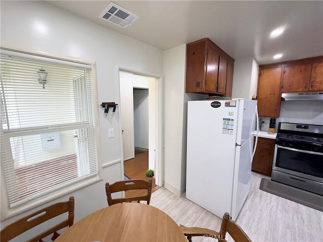kitchen with freestanding refrigerator, under cabinet range hood, visible vents, gas range, and light wood-type flooring