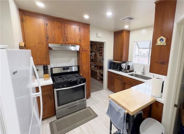 kitchen featuring freestanding refrigerator, under cabinet range hood, stainless steel gas stove, visible vents, and a sink