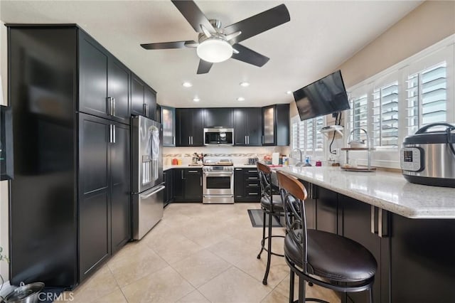 6253 Hamilton Ct, Chino, CA 91710 - kitchen featuring stainless steel appliances, ceiling fan, light stone countertops, light tile patterned flooring, and dark cabinets