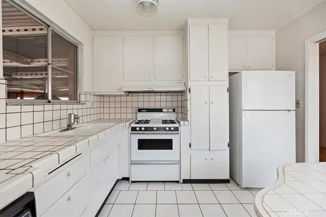 kitchen featuring white cabinets, backsplash, tile countertops, and white appliances