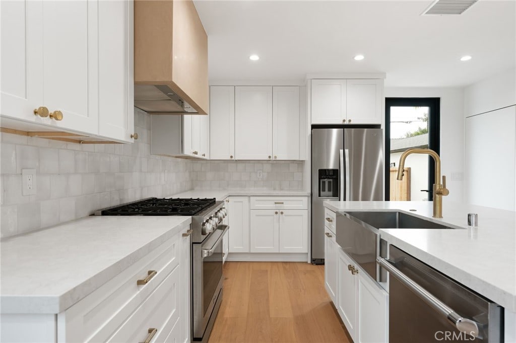 kitchen featuring light countertops, a sink, visible vents, wall chimney range hood, and appliances with stainless steel finishes