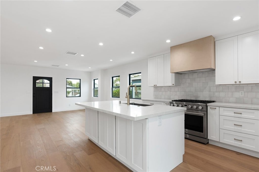 kitchen with premium range hood, a sink, a kitchen island with sink, visible vents, and high end stainless steel range oven