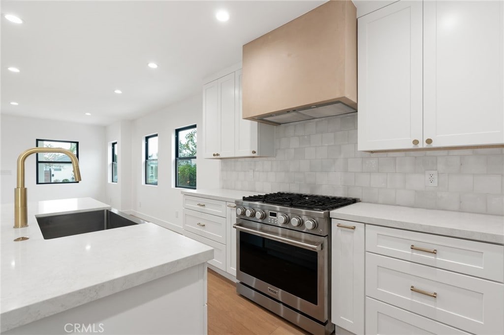 kitchen featuring premium range hood, white cabinetry, decorative backsplash, and stainless steel stove