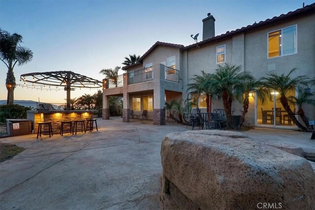 200 Cross Rail Ln, Norco, CA 92860 - back of house at dusk featuring a chimney, a patio area, stucco siding, and a balcony