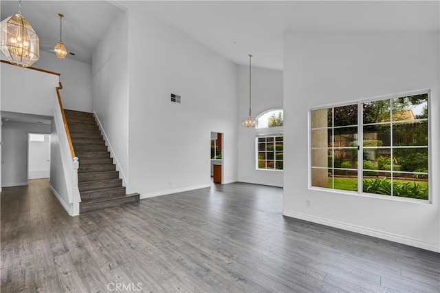 unfurnished living room featuring a notable chandelier, visible vents, high vaulted ceiling, wood finished floors, and stairway