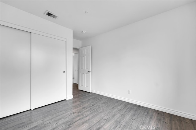 unfurnished bedroom with a closet, visible vents, wood finished floors, and baseboards