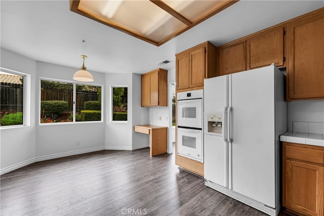 kitchen with brown cabinetry, white appliances, pendant lighting, and dark wood-style floors