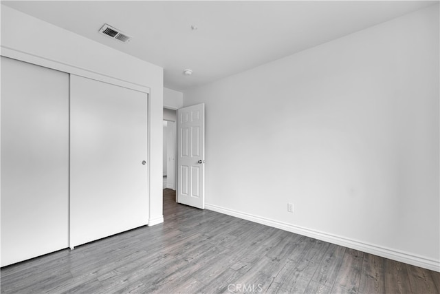 unfurnished bedroom with a closet, visible vents, wood finished floors, and baseboards