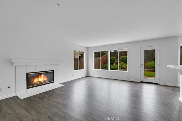 unfurnished living room with baseboards, a tile fireplace, and wood finished floors