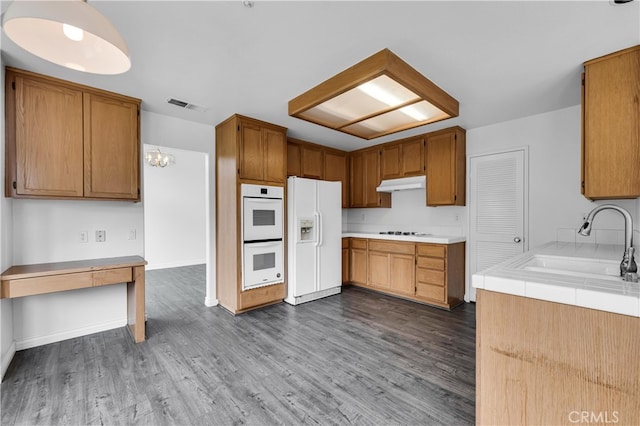 kitchen featuring a sink, visible vents, dark wood-style flooring, white appliances, and under cabinet range hood